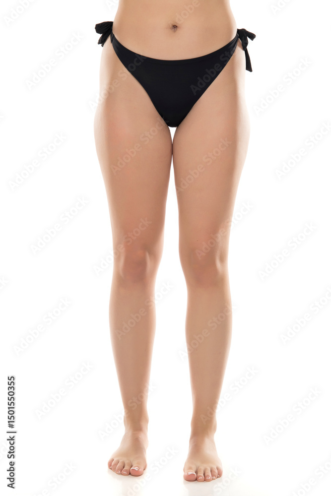 © vladimirfloyd - Close-up view of woman wearing black bikini bottom with side ties against white background, natural figure, swimwear fashion detail, lower body portrait