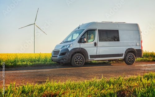 white commercial van on road between rapeseed fields with view to wind generator