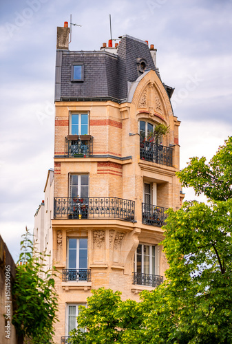 Fototapeta Naklejka Na Ścianę i Meble -  Multi-storey narrow residential building in Paris (France) with wrought-iron balustrades, small balconies, sandstone façade and sloping roof. Typical old building in the streets of the french capital.