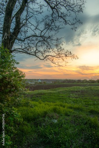 Evening Landscape with Field, Village, and Dramatic Sunset
