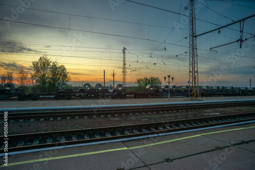 Freight Train with Coiled Steel Cargo on Tracks at Sunset