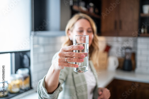 Foto Woman holding glass of fresh water in kitchen promoting hydration and healthy li