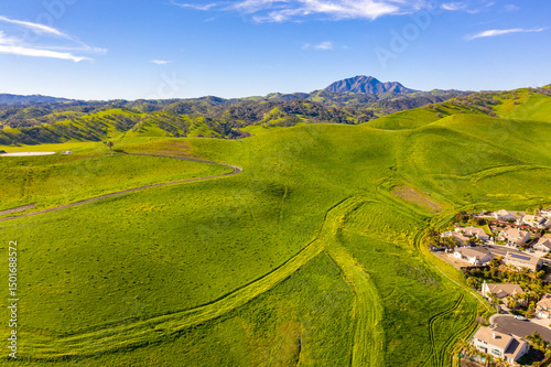 Wide aerial panorama over Antioch, CA, showing suburban rooftops stretching to the delta with clear skies, windmills in the distance, and solar energy visible on rooftops throughout the neighborhood.