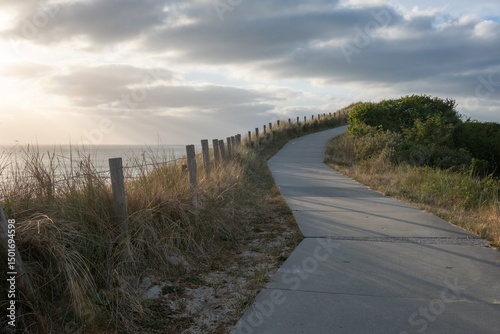 Fototapeta Naklejka Na Ścianę i Meble -  Winding paved path along coastal dunes at sunset with dramatic sky