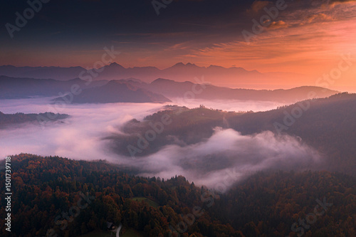 Aerial view of misty mountains and lush forest under a beautiful sunset, Spodnja Lusa, Skofja Loka, Slovenia. photo