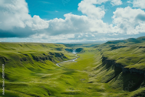 Lush green canyon landscape with distant waterfall under a cloudy sky