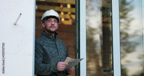 Wallpaper Mural Construction worker holding blueprints, looking upward with focus, wearing hard hat, standing in doorway of unfinished building, representing planning and architectural inspection Torontodigital.ca