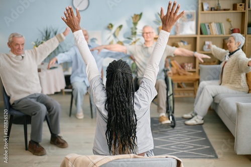 Instructor leading group exercise with senior participants seated in living room setting. Highlighting active engagement, this scene captures enthusiasm and focused commitment