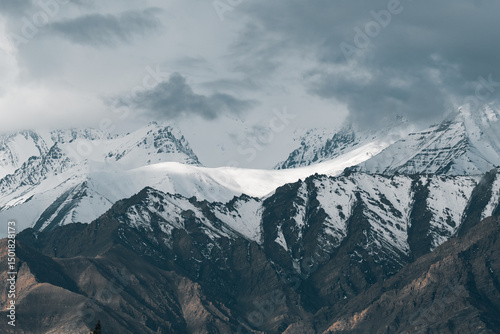 Majestic snow-covered peaks of the Himalayas rising through dramatic clouds, showcasing the raw beauty and grandeur of the world highest mountain range in its wild, untamed glory photo