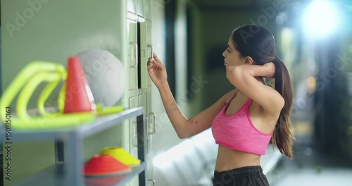 Indian asian young adult gen z tired woman lady walk in changing room open lockable cupboard picking t shirts towel wipe off sweat female girl standing taking break from warm up club