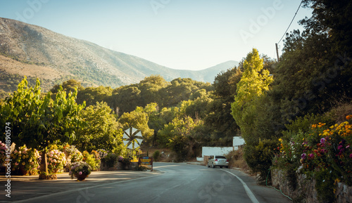 Driving around Lasithi Plateau. Empty mountain road in the afternoon - driver's point of view. Narrow road in montane rural area surrounded with lots of trees and blooming shrubs. photo