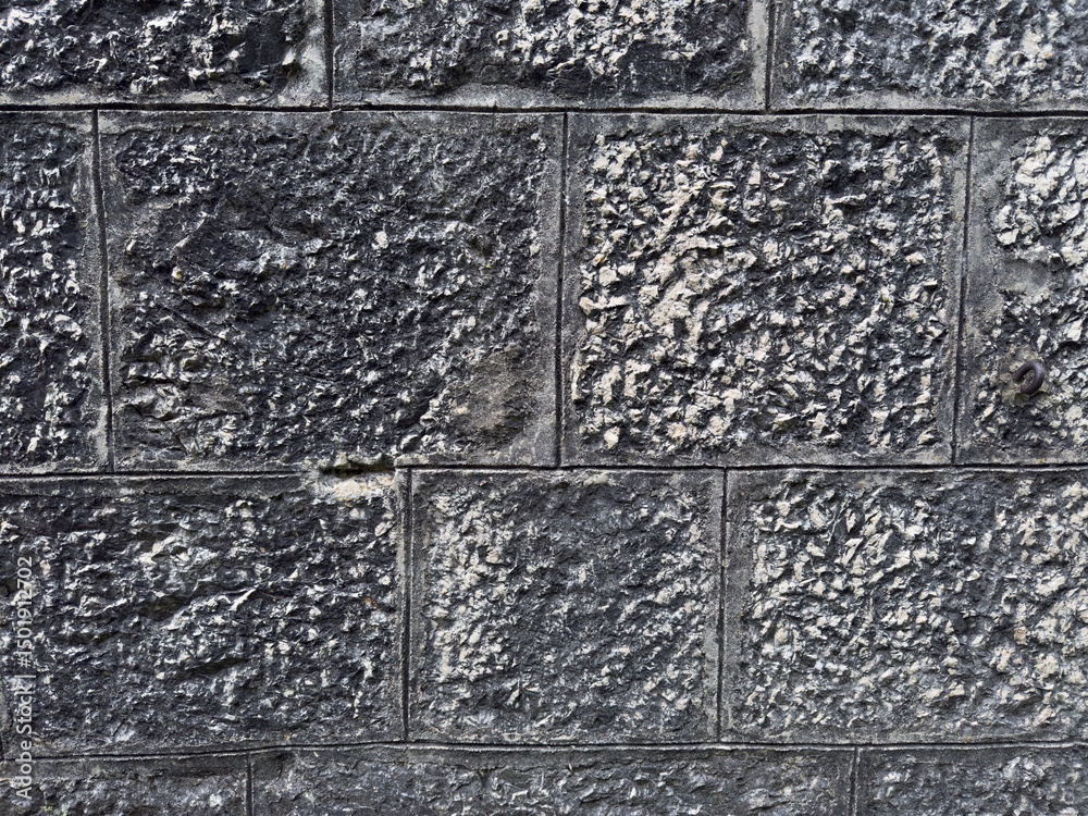 Fototapeta premium Close up of a dark textured stone wall featuring square blocks with weathered surfaces and defined joints