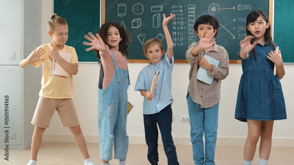Fototapeta premium Multicultural elementary student in casual cloth looking at camera while waving hands at classroom. Group of diverse children hold notebook and smiling to camera at blackboard in classroom. Pedagogy.
