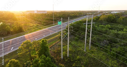 Electric transmission towers with high voltage lines crossing above highway traffic. Infrastructure concept for energy distribution and road network.