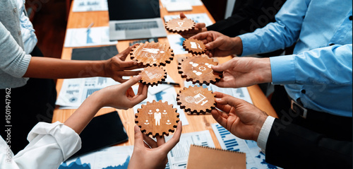Photos A diverse group of hands holds wooden gears depicting business icons in a collaborative office meeting, symbolizing teamwork and strategic planning for success