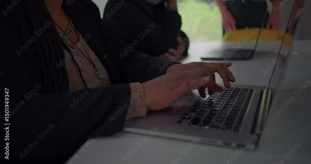 Hands typing on laptop keyboard during office meeting as camera slowly reveals African American businesswoman working at shared table with colleagues Hands typing on laptop keyboard during office meeting as camera slowly reveals African American businesswoman working at shared table with colleagues