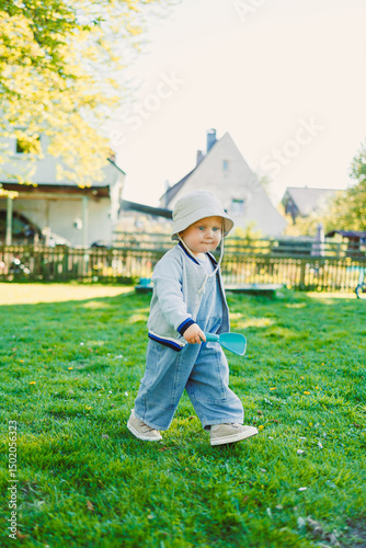 Cute boy running on the grass in a stylish shirt and sunbathing in the sun. Carefree childhood with joyful laughter of a child. Toddler having fun and enjoying a walk in nature.