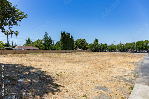 Vacant lot in a suburban Antioch, California neighborhood on a sunny day. The dry land and sparse grass suggest development potential or urban infill opportunity near residential housing.