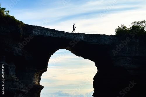 Silhouette of person walking on natural rock arch bridge