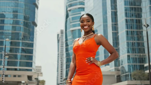 Elegant woman in orange dress standing in front of the city skyscraper. The woman radiates confidence
