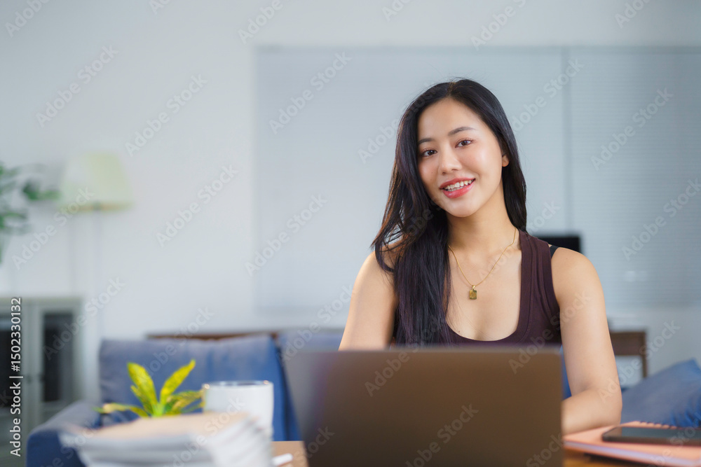 Happy Asian woman working remotely from her cozy home, smiling while typing on her laptop and enjoying a productive day Happy Asian woman working remotely from her cozy home, smiling while typing on her laptop and enjoying a productive day