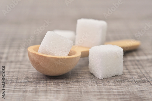 Cube sugar in woonden spoon on table background. Sugar type  are fructose, glucose, lactose. Over consumption can be weight gain, type 2 iabetes and heart disese.