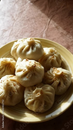 Steaming fresh bao buns topped with sesame seeds arranged on a plate in soft lighting on a neutral background