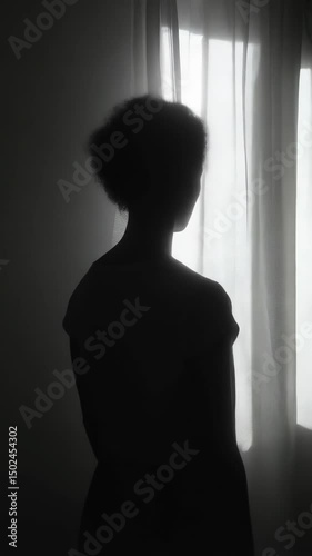 Silhouette of a woman standing by a window with sheer curtains in a dimly lit room, creating a soft contrast