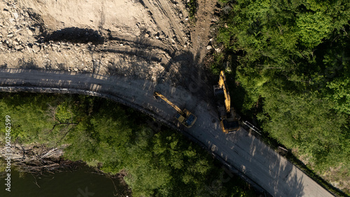 Top-down drone shot of Vernasca SP21 at Mignano Dam shows landslide debris covering the road with excavators working at the edge, trees and dam at bottom of frame, static overhead drone, real time