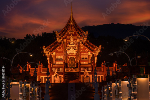 The magnificent Ho Kham  pavilion at Royal Park Rajapruek  in Chiang Mai , beautifully illuminated against a fiery sunset, showcasing exquisite Thai architecture and cultural grandeur.
