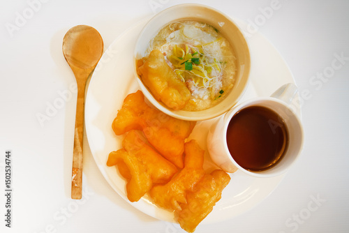 Traditional Thai breakfast with rice porridge, deep-fried dough sticks, and a hot drink. Comforting morning meal served warm with herbs and crispy toppings for flavor.