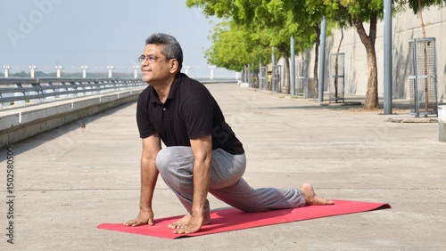 Senior Indian Man performing Ashwa Sanchalanasana (Equestrian Pose) outdoors on a yoga mat, focusing on flexibility, balance, and mindful breathing during morning yoga routine at riverfront Ahmedabad 