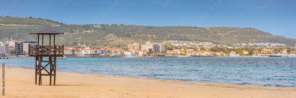 Obraz premium Picturesque beachfront scene featuring a lifeguard tower overlooking a serene coastline and a charming town nestled against lush green hills