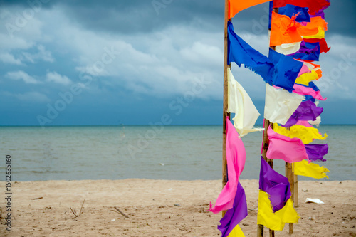 Wooden poles with cloth tied in various colors on the beach and the sea in the background.