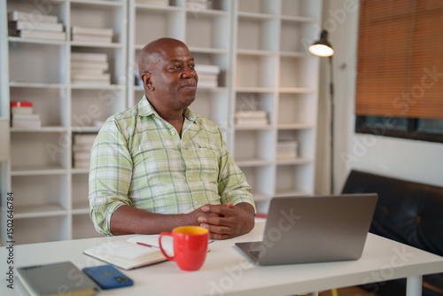 Wallpaper Mural Confident mature african american entrepreneur sitting at desk in home office looking away and thinking about new business ideas while working remotely using laptop and notebook Torontodigital.ca