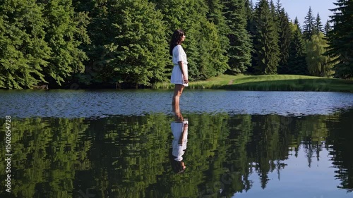 Woman standing on water surface reflecting trees in serene natural setting at lakeside