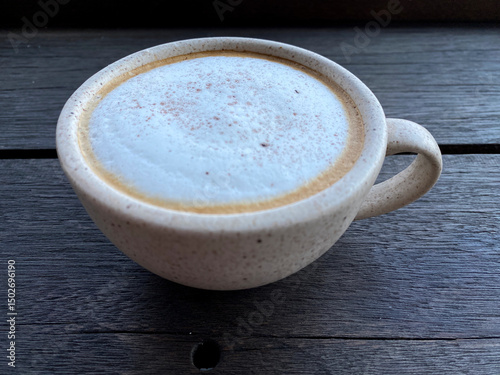 Hot cappuccino coffee in white cup on wooden table background. Art of milk foam circle shape with copy space on brown melt coffee top view