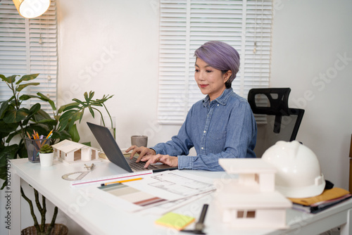 Asian Woman Architect Designs House on Laptop Architect at Desk Designs Blueprint Asian Woman Working on House Project Using Laptop for Design Plan
