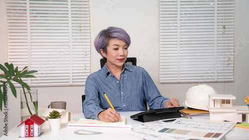 Asian Older Woman Architect Working on Blueprint Design and Building Model at Office Architect and design house building concept with blueprints