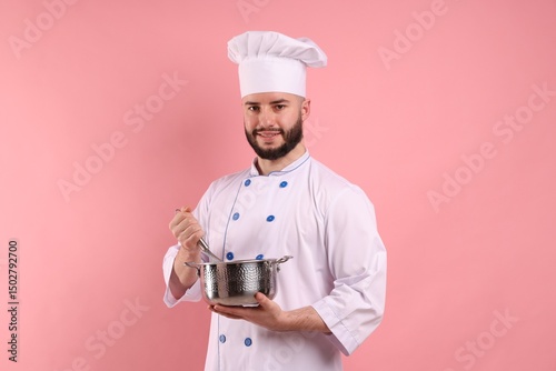 Quadro su tela Happy confectioner in uniform holding whisk and cooking pot on pink background