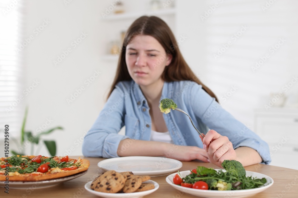 Sad teen girl holding fork with broccoli at home, selective focus. Eating disorder Sad teen girl holding fork with broccoli at home, selective focus. Eating disorder