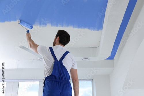 Foto Man painting white ceiling with blue dye indoors, low angle view