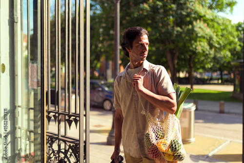 Indian businessman is walking out of a store, holding a reusable shopping bag filled with fresh vegetables, promoting a sustainable lifestyle
