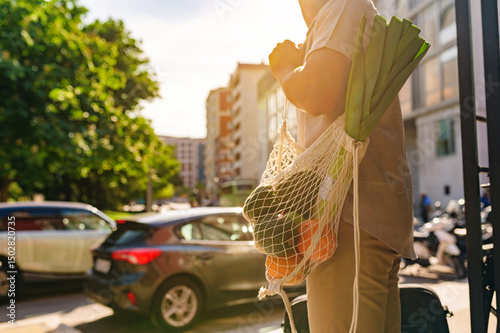 Indian businessman walks down a city street, carrying a reusable shopping bag filled with fresh groceries, promoting sustainability