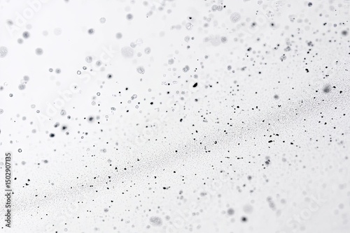 Abstract image of tiny, dark particles dispersed across a white background.  Particles varying in size and density, creating a sense of depth and motion