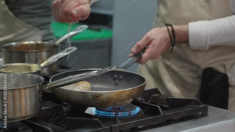 Professional chef working in a commercial kitchen preparing a meal with steam rising from the cooking pans and other kitchen equipment visible The chef is focused on the cooking process, pouring sauce Professional chef working in a commercial kitchen preparing a meal with steam rising from the cooking pans and other kitchen equipment visible The chef is focused on the cooking process, pouring sauce
