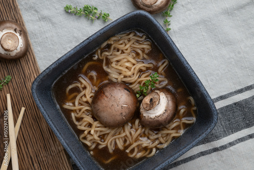Close-up view from above, mushroom and noodle soup in a black square bowl on a marbled background.