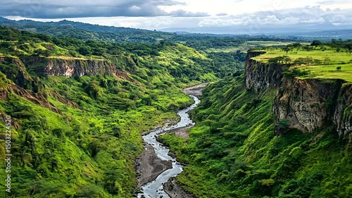 Winding river through lush canyon with green vegetation & stunning cliff formations under a cloudy sky