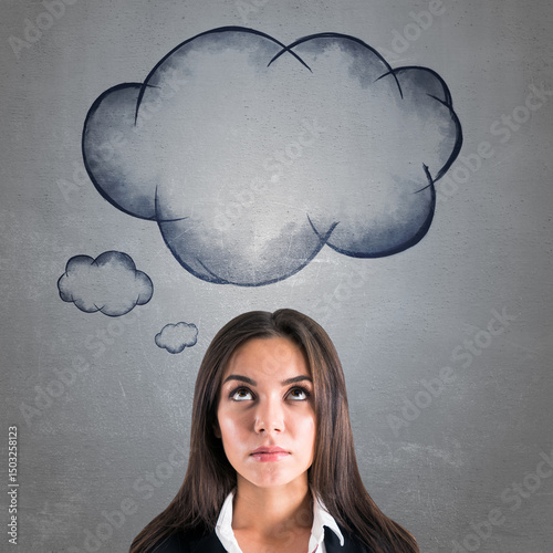 Young businesswoman in formal attire looking up thoughtfully at large hand-drawn thought clouds on a textured gray wall background conceptually.