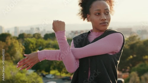 A young woman stretches her arms before exercising in a park overlooking a city. She is preparing for her workout.